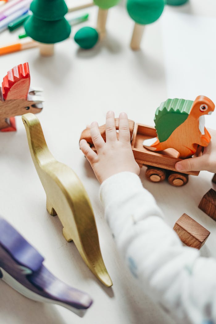 Services Child's hands interact with vibrant wooden toy dinosaur set, creating playful scene on tabletop.