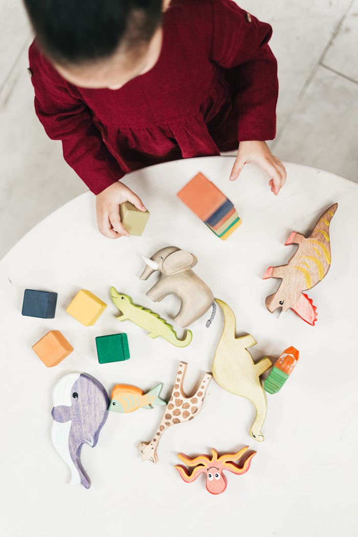 About A young girl in a red dress playing with wooden animal toys on a round table, viewed from above.